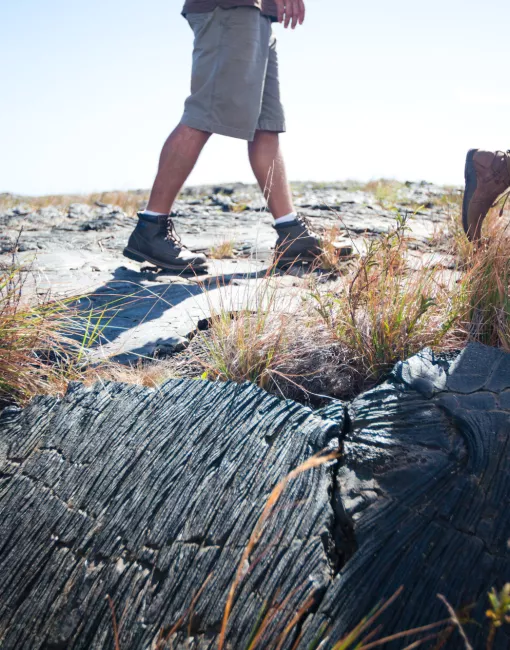 Person hiking on a rocky path surrounded by dry grass, focusing on their boots and the trail.