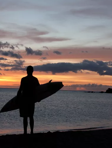 Silhouette of person holding a surfboard on the beach