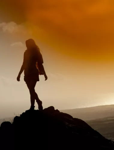 Silhouette of a hiker at sunrise with scenic mountain and forest backdrop.