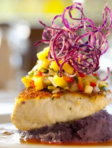 Seared fish fillet topped with tropical fruit salsa, garnished with spiraled vegetables, served on purple mashed potatoes