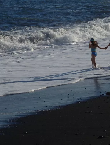Children playing near the waves on a black sand beach in the Kalapana area on the southeastern coast of Hawaii.