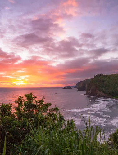 Scenic view from Pololu Valley Lookout at sunset, overlooking a lush valley, black sand beach, and the northeastern coastline.