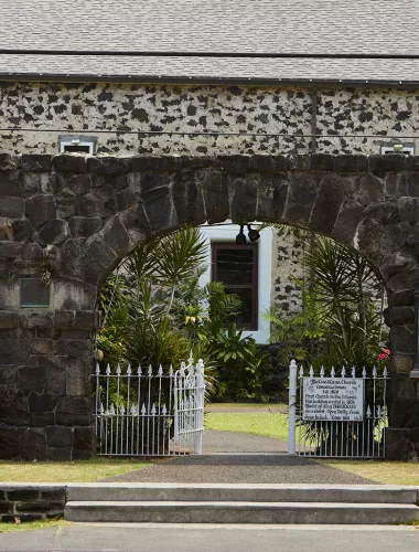 Historic Kailua Village (Kailua-Kona) Stone building and white gate in Historic Kailua Village, surrounded by tropical greenery.