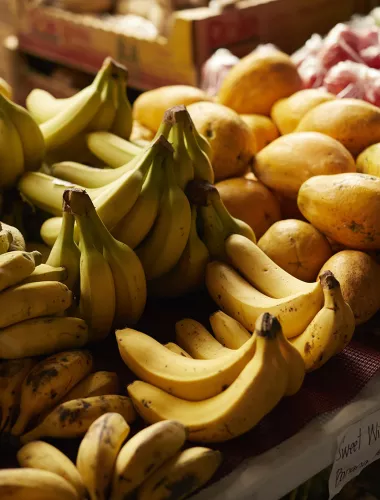 Fresh bananas and papayas displayed on a market stand.