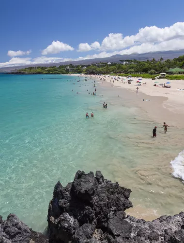 Wide view of Hapuna Beach with turquoise waters, white sand, and visitors enjoying the shoreline on a sunny day.