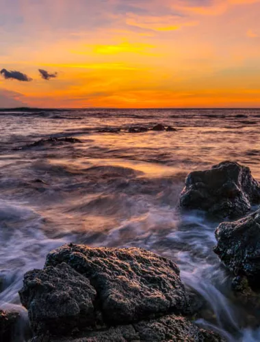 Ocean sunset with waves crashing against rocks in the foreground
