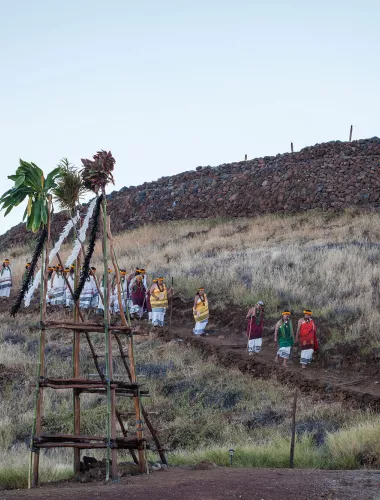 Puukohola Heiau National Historic Site Visitors walking toward Puukohola Heiau, a historic temple surrounded by dry grassland under a clear blue sky.
