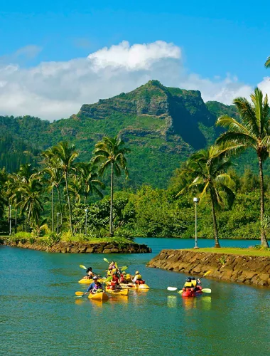 A serene river bordered by palm trees and lush greenery, with kayakers paddling in calm waters.