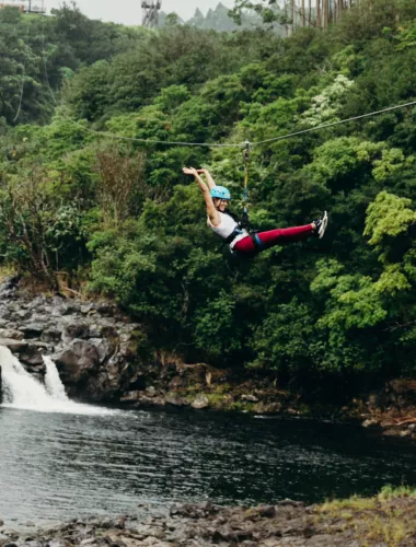 Person ziplining over lush green forest and river gorge.