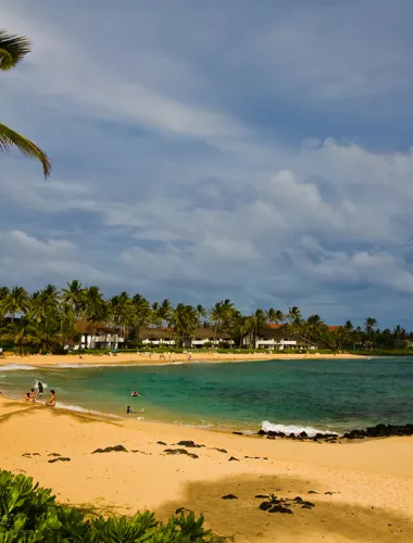Poipu Beach Park with golden sand and clear water surrounded by lush greenery.