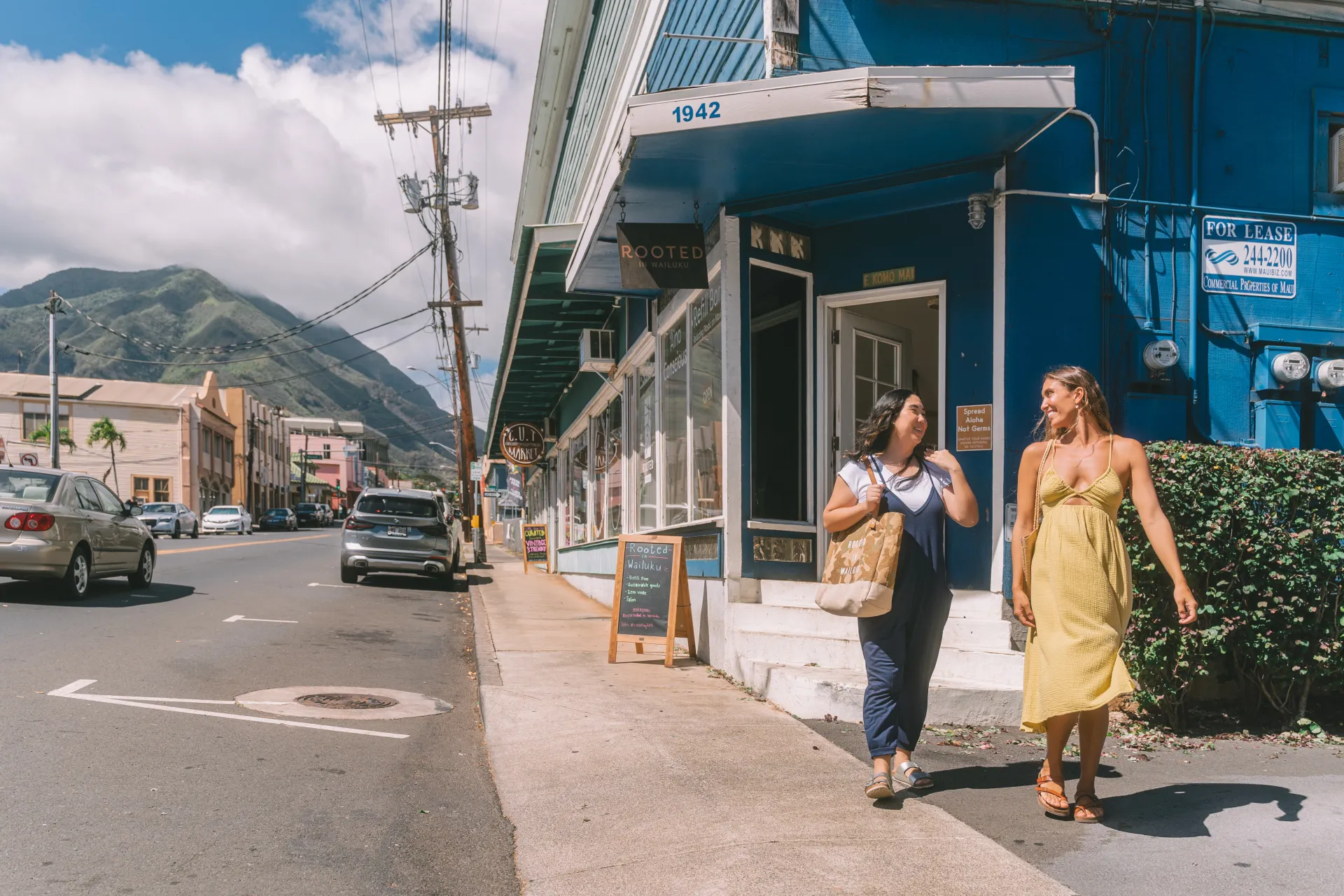 Two women walking down the sidewalk along store fronts with shopping bags in their hands
