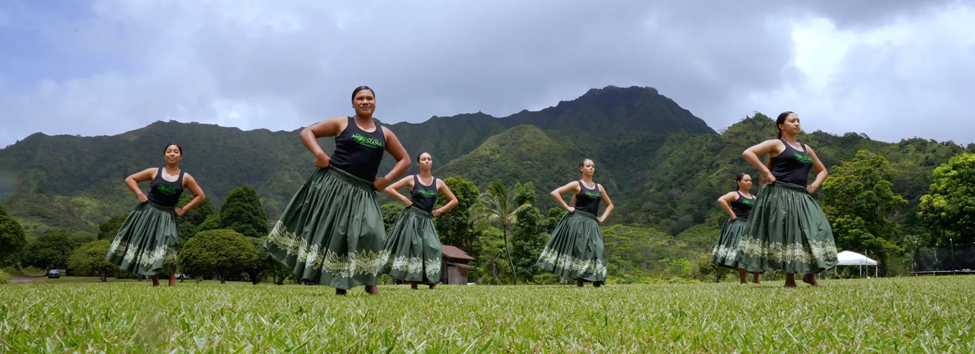 Kumu Hula Leināʻala Pavao Jardin and her hula dancers in a grassy field in Hawaii