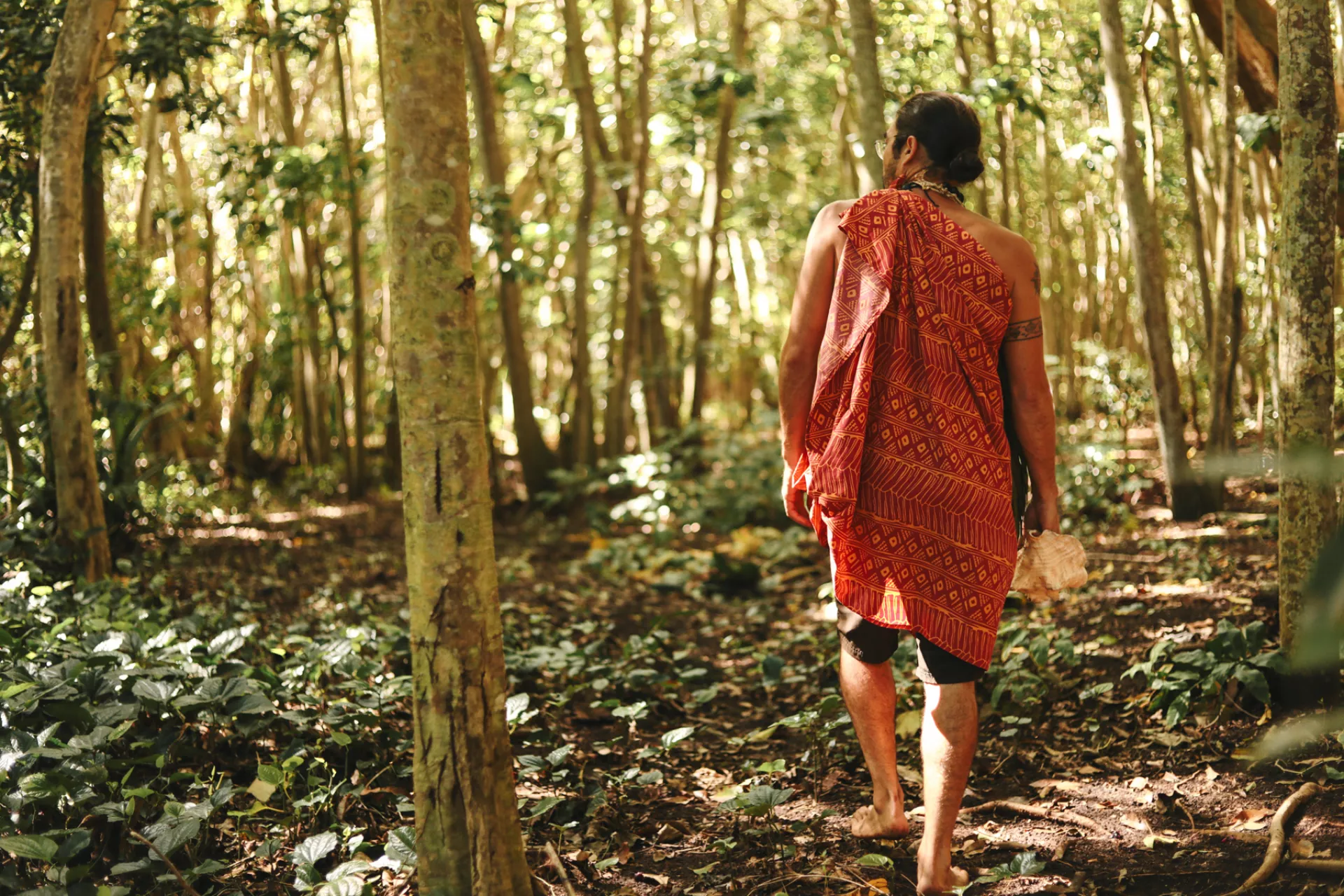 A man in cultural garb walks through a forest on the island of Molokai.