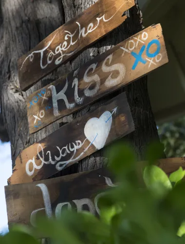 Wooden signs on a tree with words like Together, Kiss, and Always, decorated with hearts.