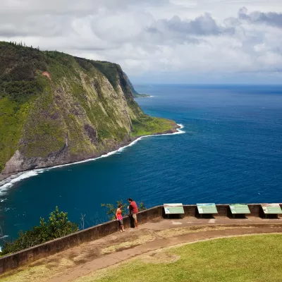 Waipio Valley Lookout Couple enjoying a scenic view of steep green cliffs and the deep blue ocean at Waipio Valley Lookout.