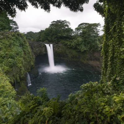 Rainbow Falls cascading into a pool surrounded by dense tropical vegetation.