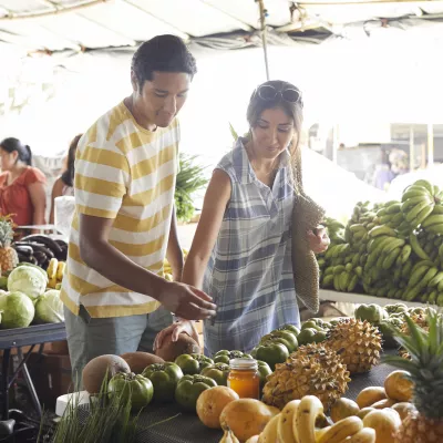Couple browsing fresh fruits and vegetables at an outdoor farmers market in Hilo.