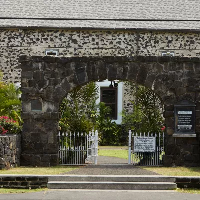 Stone building and white gate in Historic Kailua Village, surrounded by tropical greenery.