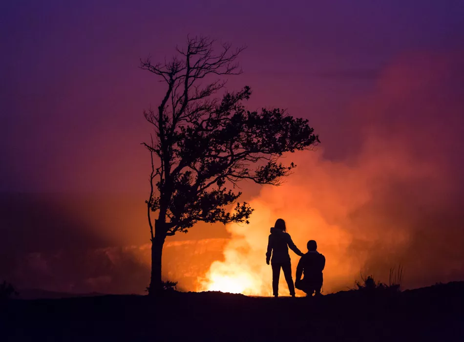 Silhouettes at sunset near an erupting volcano in Hawaii Volcanoes National Park.