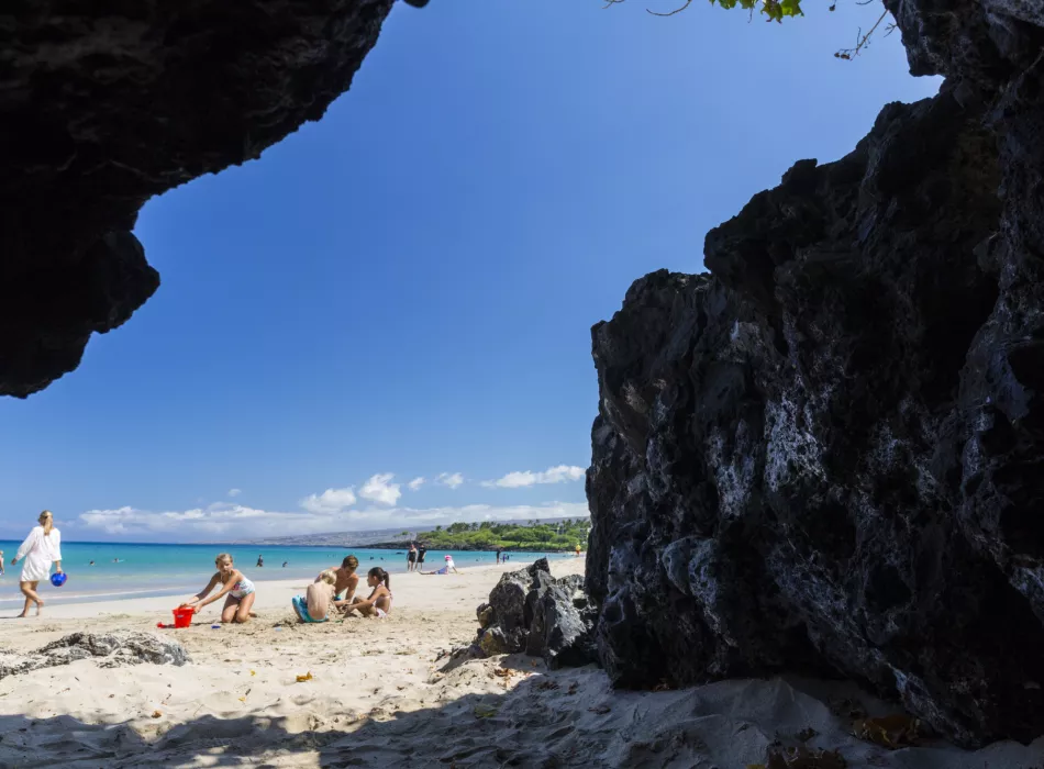 View of Hapuna Beach with white sand, clear blue skies, and families enjoying the shore.