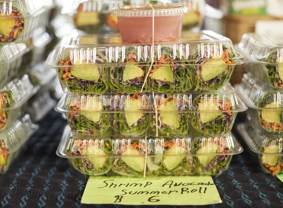 Stacked containers of shrimp avocado summer rolls with dipping sauce on display.