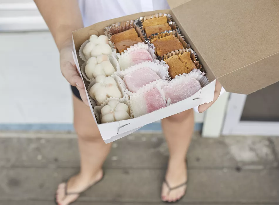 Box of assorted mochi and Japanese confections held by a person, showcasing a variety of textures and colors.