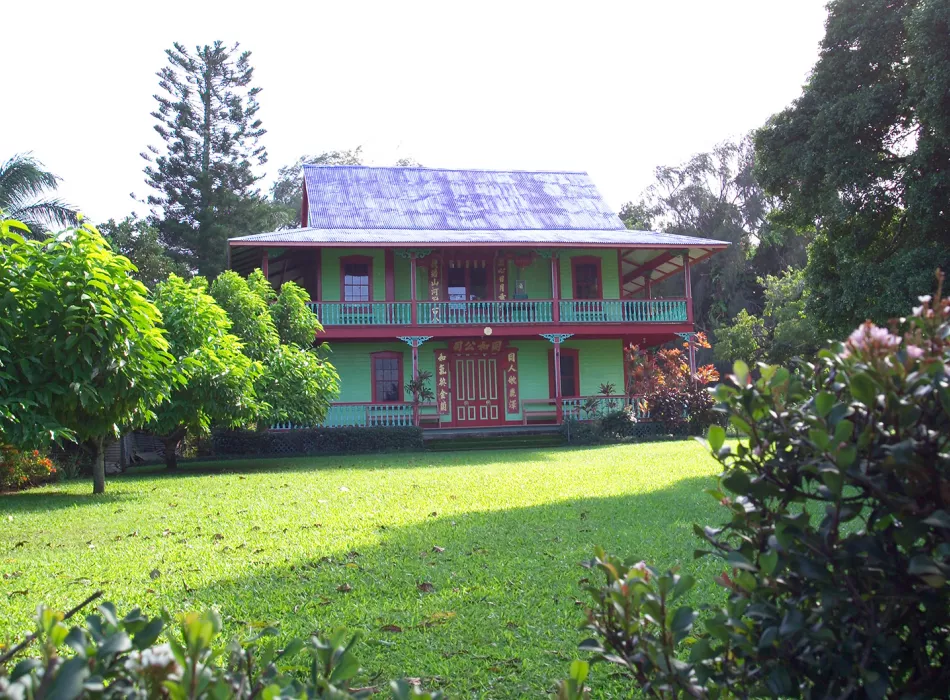 Charming two-story green house with red trim surrounded by lush greenery and a manicured lawn in the peaceful town of Hawi.