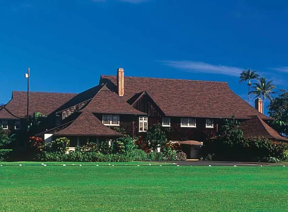 A historic plantation house surrounded by lush green lawns, tropical plants, and palm trees under a clear blue sky.