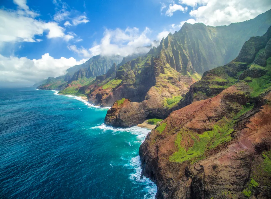 A breathtaking view of Hawai‘i’s Napali Coast with rugged green cliffs meeting the deep blue ocean.