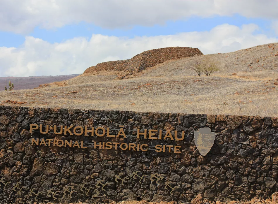 Puukohola Heiau National Historic Site with a large stone heiau structure set on a dry, grassy landscape under a partly cloudy sky.